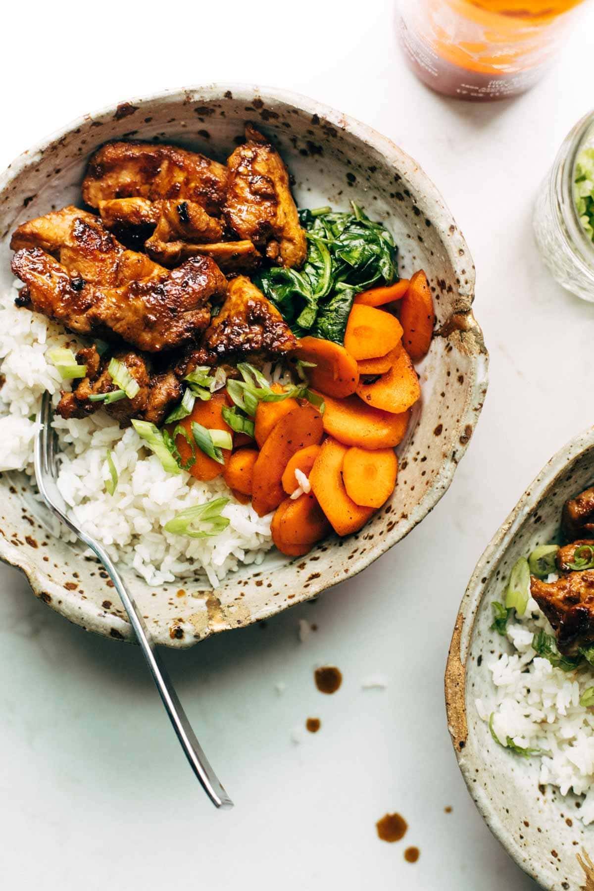 Spicy pork in a bowl with veggies and rice.