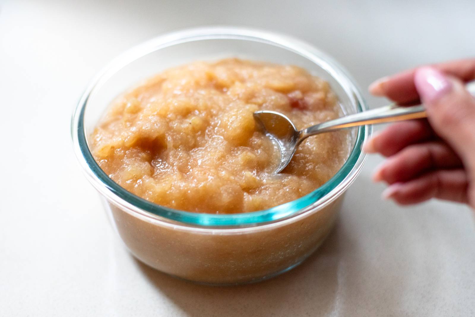 Applesauce in a glass bowl with a spoon.