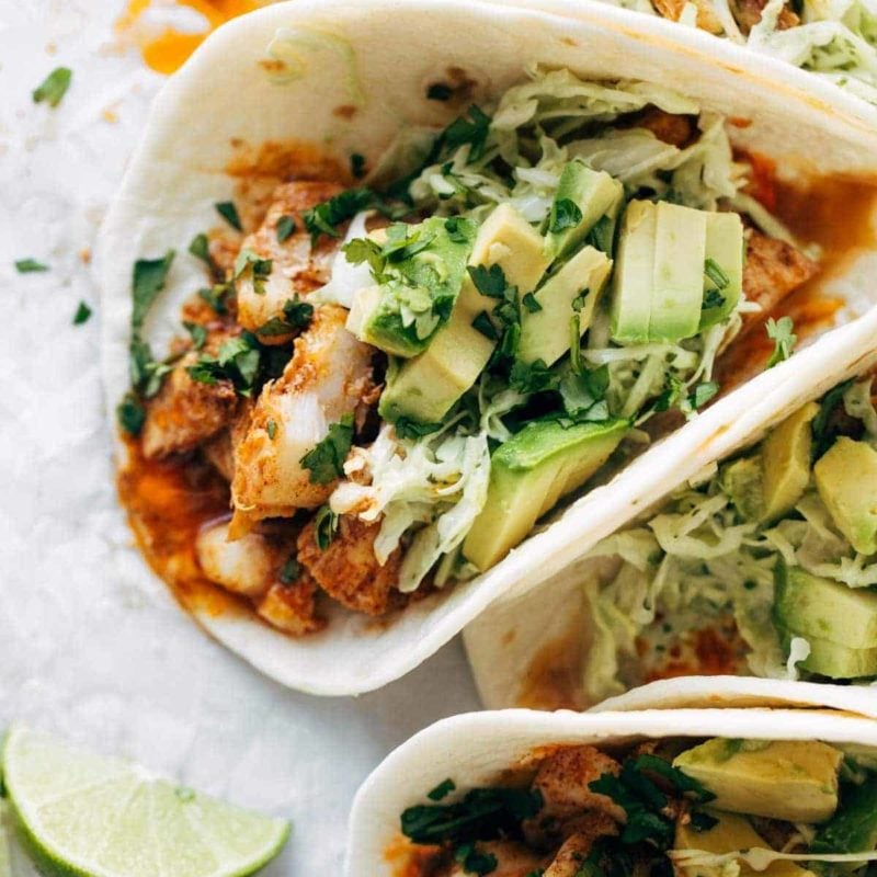 Fish tacos with avocados and a wedge of lime next to them.