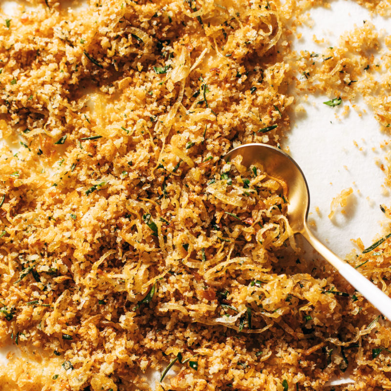 Golden breadcrumbs on a sheet pan with a spoon.