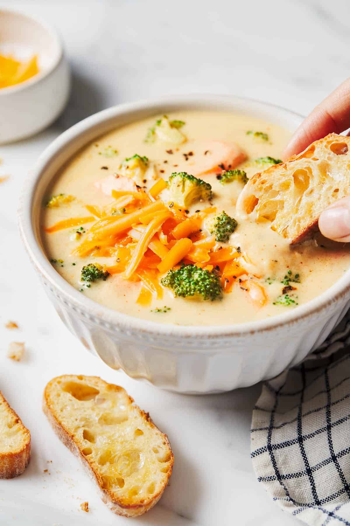 Broccoli cheese soup in a bowl with bread dipped in.