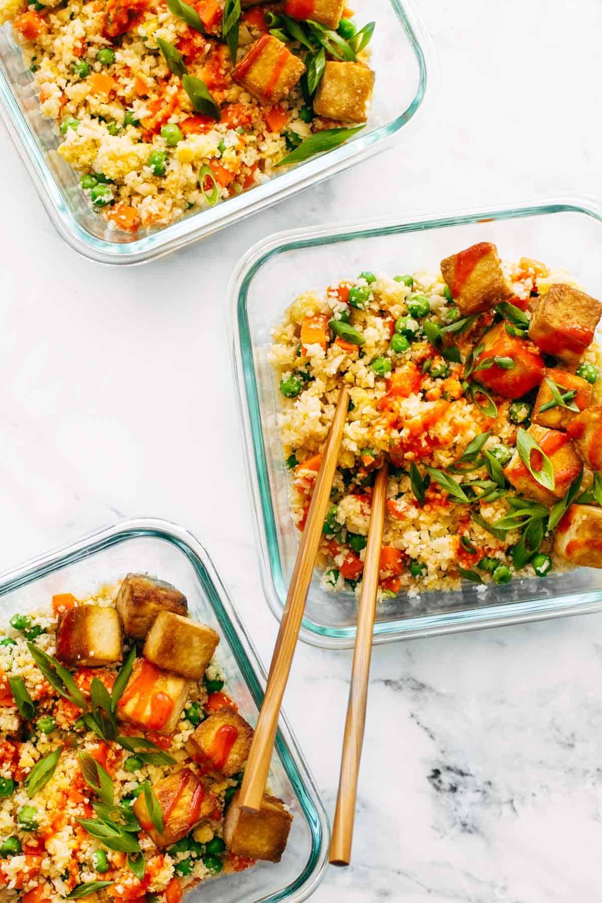 Cauliflower fried rice  in meal prep containers with chopsticks.