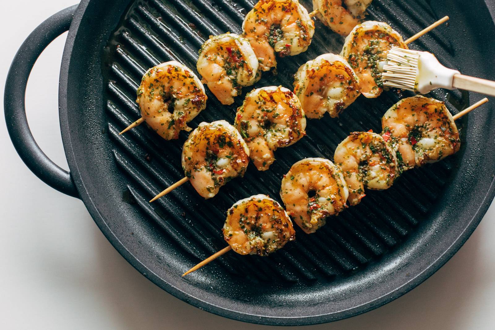 Grilling shrimp while brushing on chimichurri sauce,