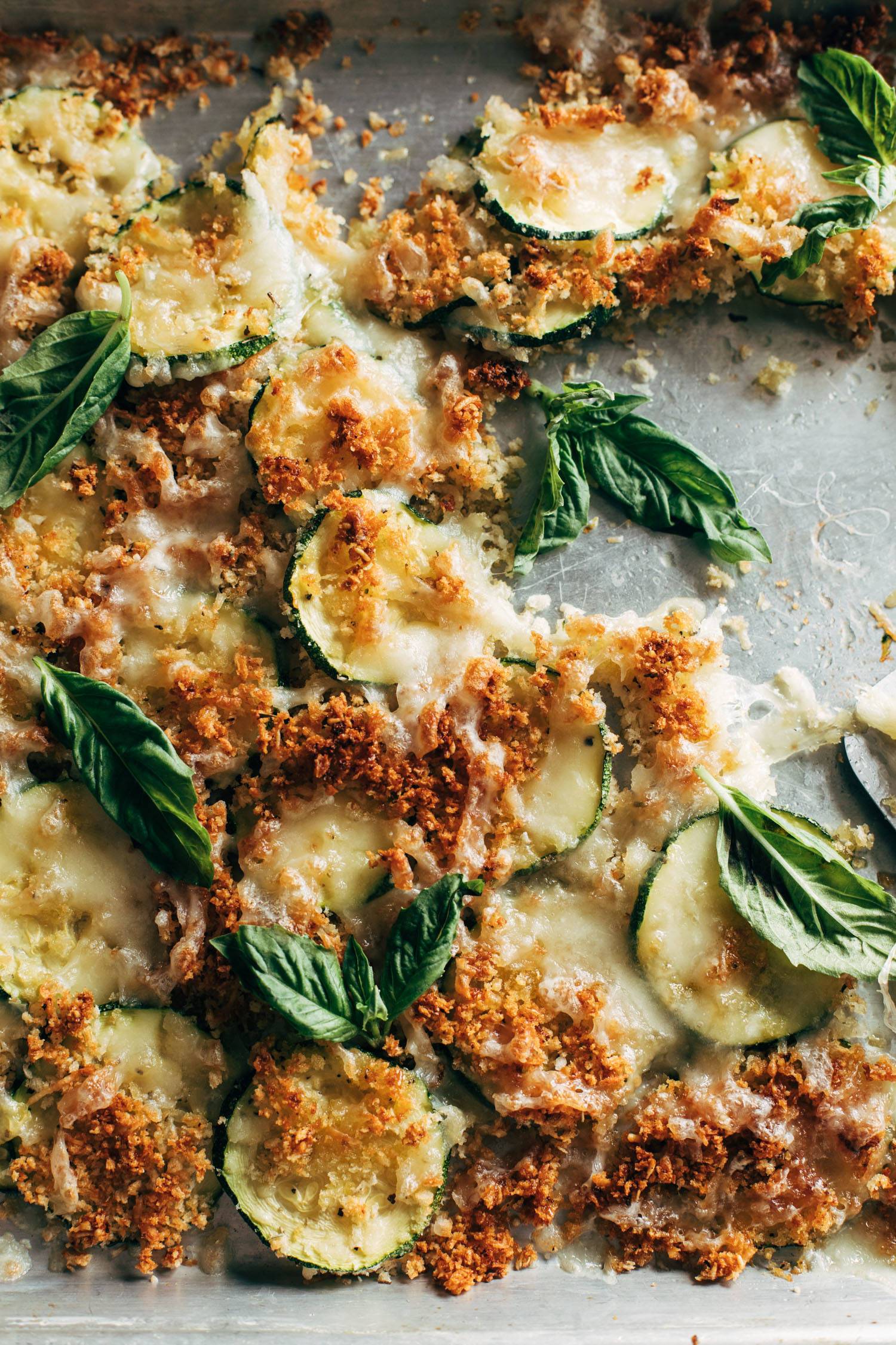 Roasted zucchini covered in breadcrumbs, melted cheese, and fresh basil on a baking sheet. 