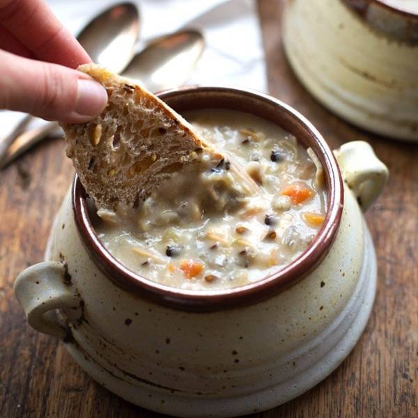 A person dipping bread into crockpot chicken wild rice soup.