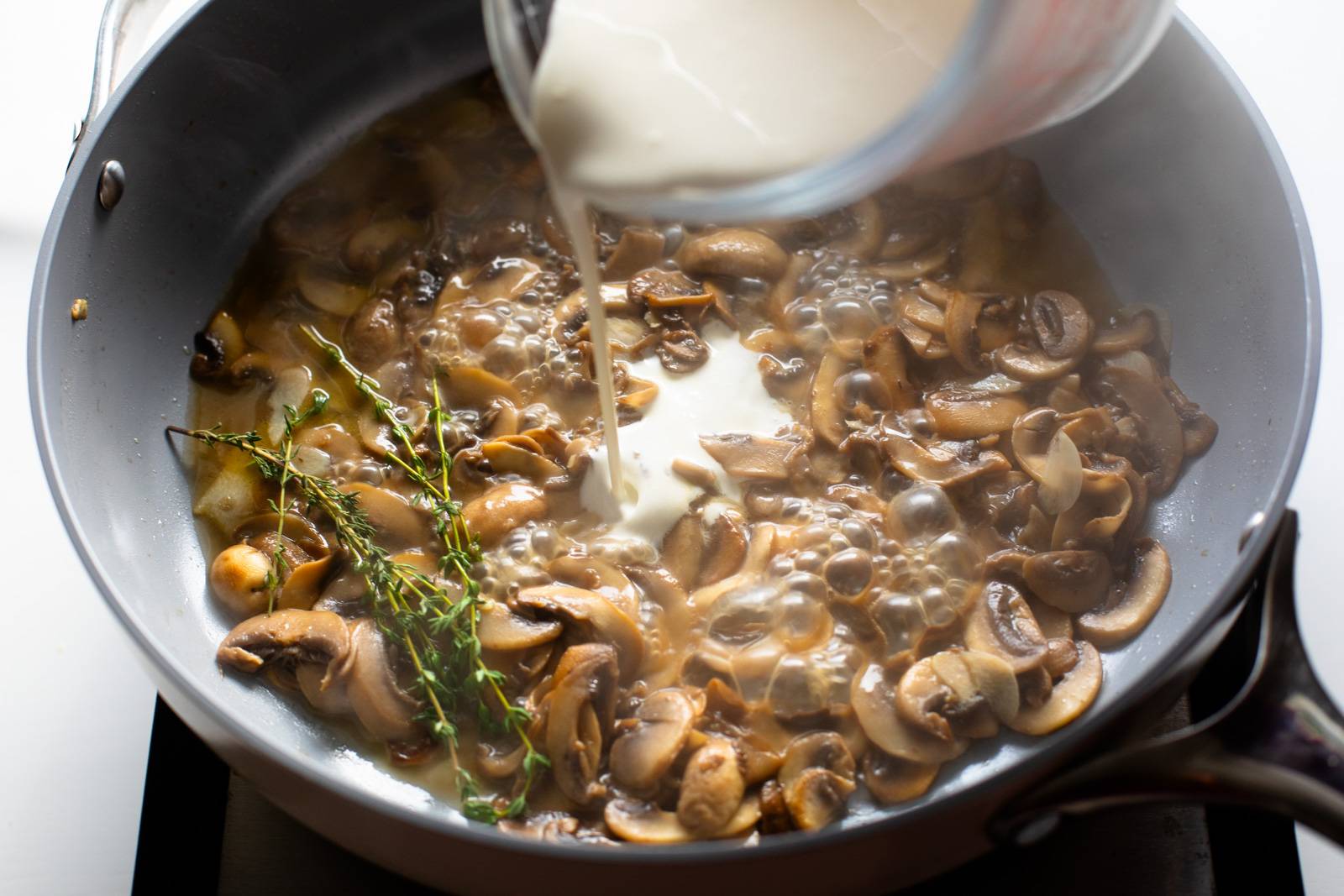 Adding cream and thyme to the pan with mushrooms.