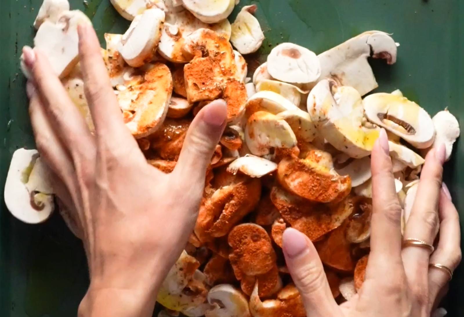 Hands mixing sliced mushrooms with oil and spices.
