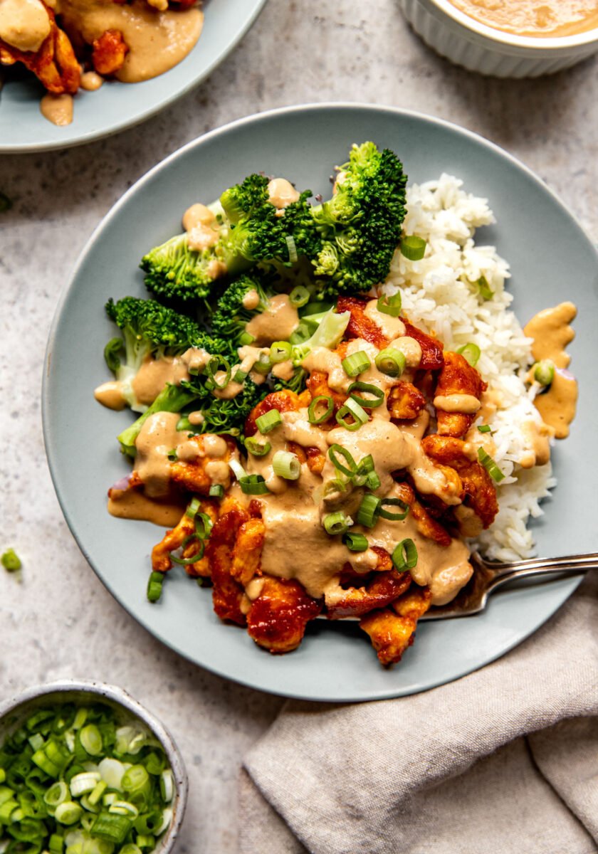 Red curry chicken stir fry on a plate with cashew sauce, broccoli, and rice
