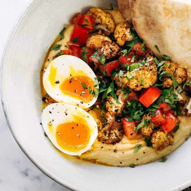 Hummus, roasted cauliflower, eggs and bread in a bowl.