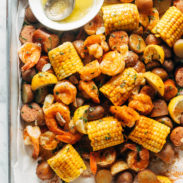 Shrimp, potato and corn mixture on a sheet pan with a side of melted butter in a bowl.
