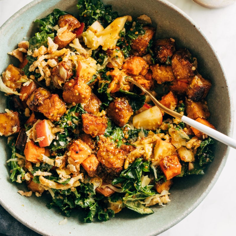 Crispy tempeh with green leafy vegetables in a bowl with a spoon.