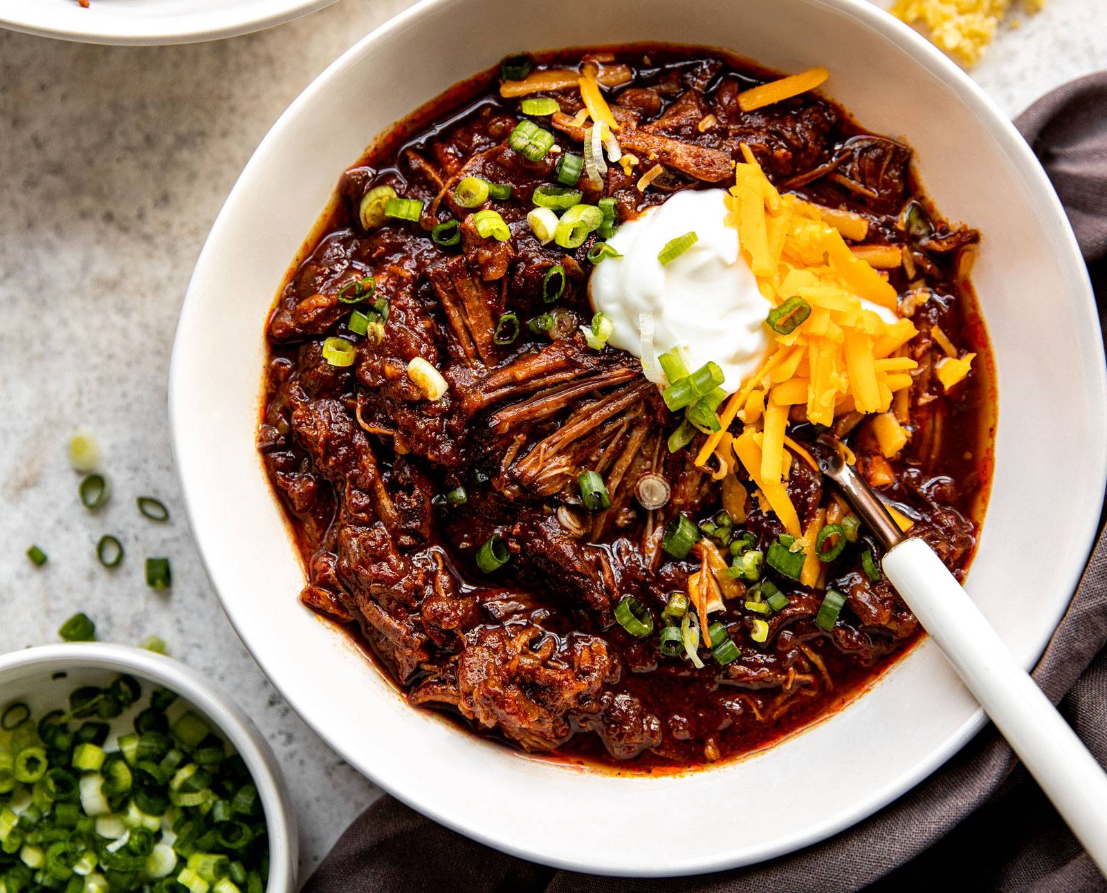 A bowl of Texas chili with sour cream, cheese, and green onions.