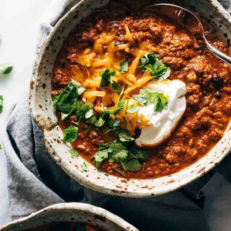 Bowls of chili with shredded cheddar, cilantro, and sour cream.