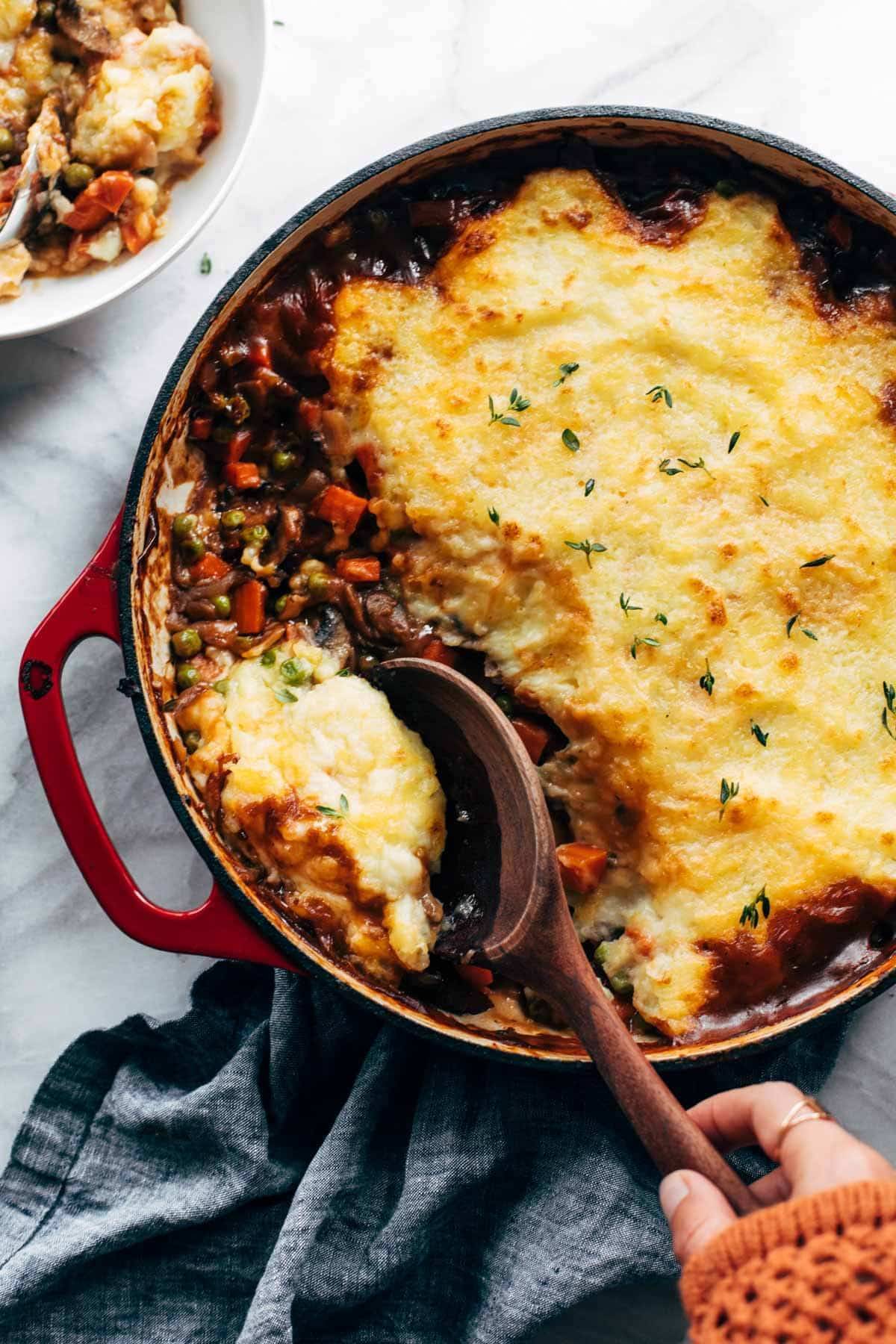 White hand scooping vegetarian shepherd's pie with a wooden spoon.