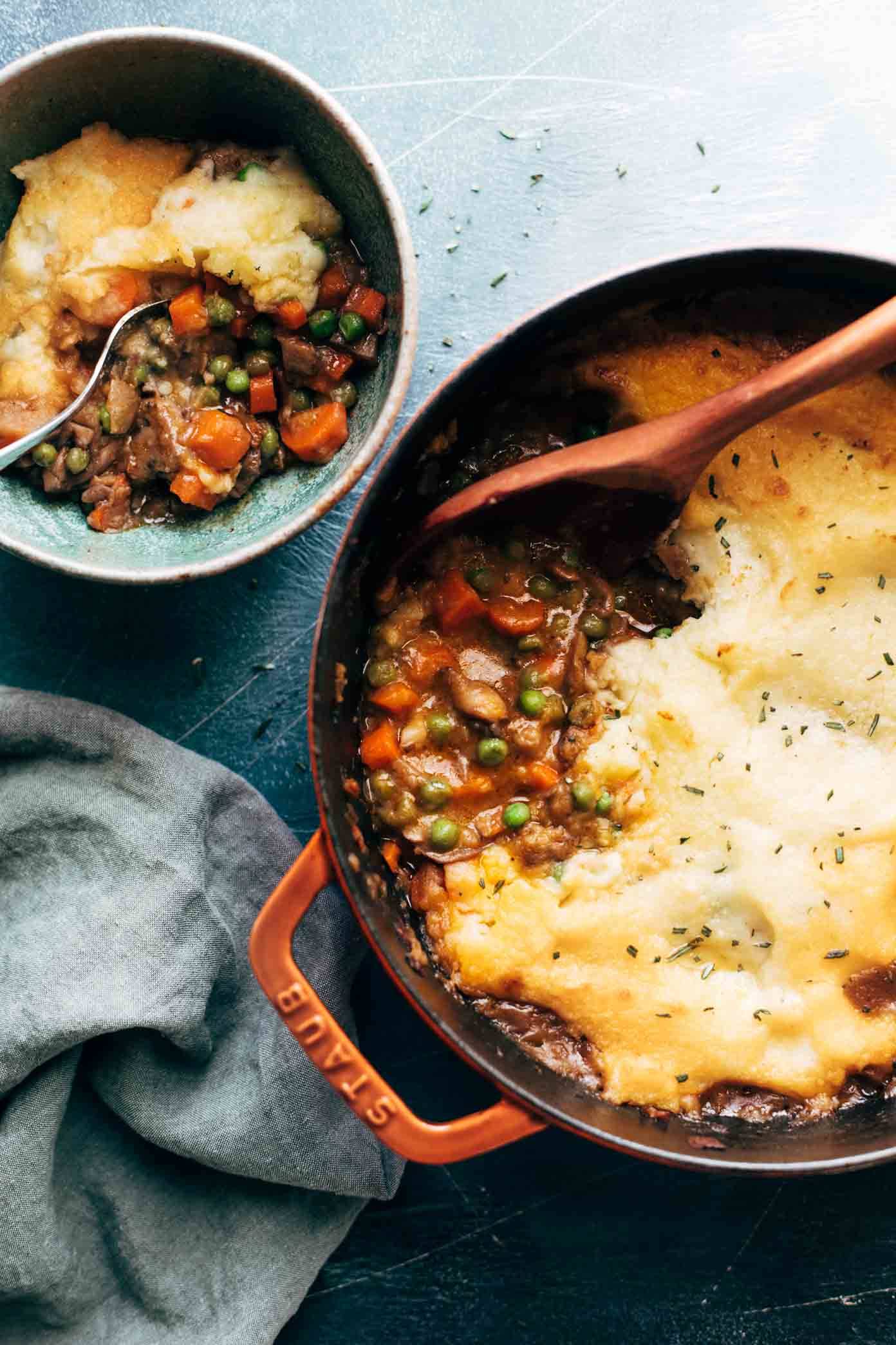 Vegetarian shepherd's pie in a pot with a wooden spoon. There's a bowl of shepherd's pie on the side.
