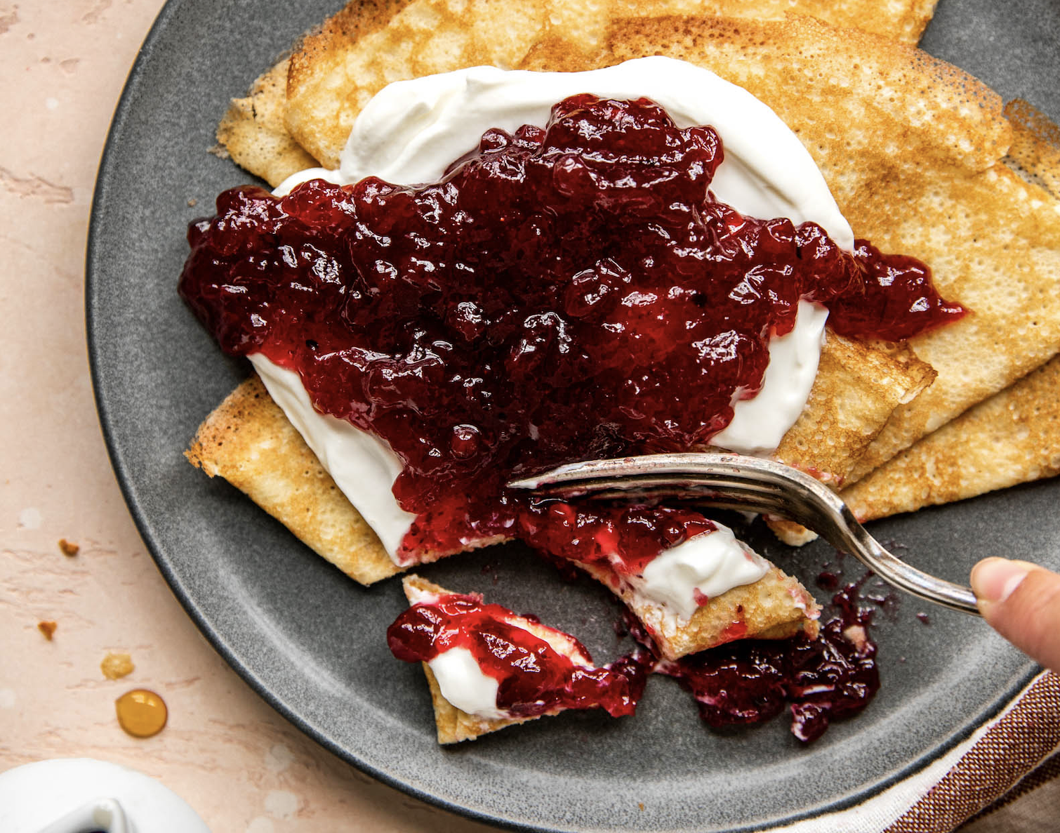Fork taking a bite out of Swedish Pancake with jam and yogurt.